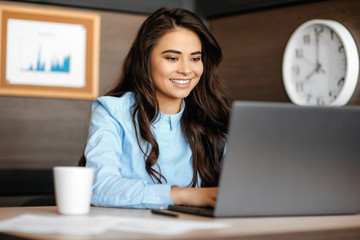 Photo of beautiful young manager woman with bright smile working with laptop in modern office.