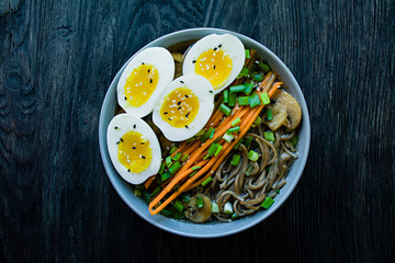 Buckwheat soba noodles with sauce and side dishes in bouillon. Japanese food. Asian cuisine. Black wooden background. View from above.