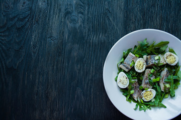 Marinated herring with arugula, onions, boiled quail eggs and lemon juice and olive oil. Delicious salad. Proper nutrition. Dark wooden background.