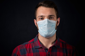 young man in a plaid shirt in a medical mask against black background