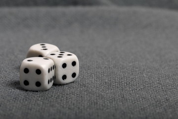 White dice with black markings. Lie on a surface covered with a coarse gray cloth