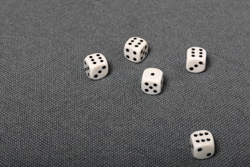 White dice with black markings. Lie on a surface covered with a coarse gray cloth