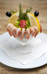 Cooked shrimps with lemon, olives and greens on a wooden background