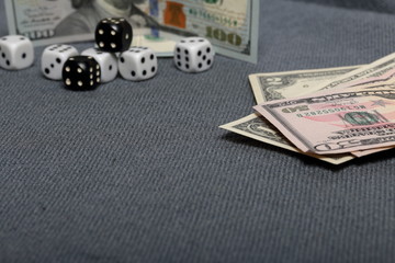 White dice with black markings. They lie on a surface covered with a coarse gray cloth. Among them are two black dice with white markings. Nearby are a few dollar bills of different denominations.