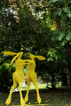 Two boxing hares on hind legs, a tall garden sculpture painted in yellow. ,Garden