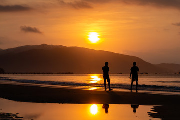 Silhouettes of people on the background of a golden dawn on the beach of Sanya, Hainan Island, China