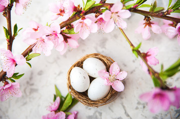 Obraz na płótnie Canvas Spring blossom concept. Easter concept, eggs in a nest, flowering tree close-up and copy space. Pink natural texture of natural flowering tree. Easter eggs and branches of blossoming on an table. Top 
