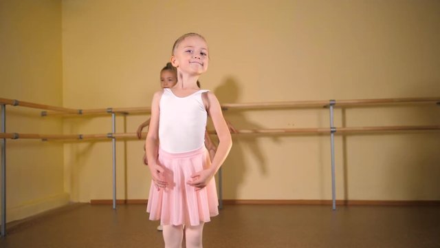 ittle ballerina in a white suit and pink skirt is engaged in a dance class