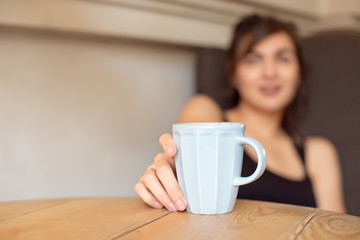 Close-up woman holding a cup of coffee sitting in a comfortable chair in a cafe