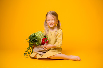 baby girl with eco bag and vegetables. baby girl blonde holding eco bag with vegetables on yellow background isolate, space for text, concept organic food