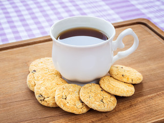 White porcelain cup with tea and sweet oatmeal cookies with pieces of dark chocolate around it on a wooden board. High-calorie breakfast.