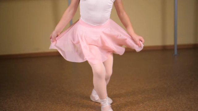 ittle ballerina in a white suit and pink skirt is engaged in a dance class