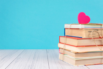 Stack of books and pink heart. Books with jute ribbon bow as gift on blue background. Education...