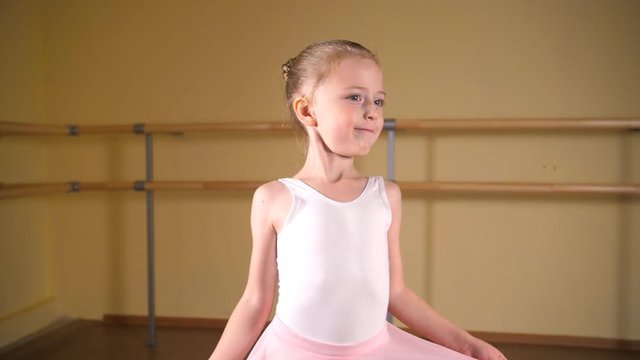 ittle ballerina in a white suit and pink skirt is engaged in a dance class