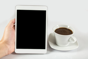 Digital tablet in one hand, on a white background next to coffee mug full of coffee, isolated