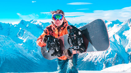 Close-up: A young guy in ski equipment is standing with a snowboard against the background of a...
