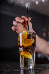 Bartender is decorating cocktail with lemon in jar with frappe at bar counter background.