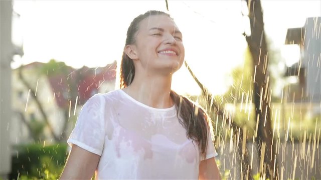 Young Smiling Woman Stands Under Fresh Rain in Summer. She Has a lot of Fun Spending Her Holidays In Nature.