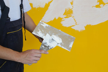 Man plastering wall with putty-knife, close up image. Fixing wall surface and preparation for painting.