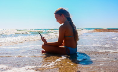 The girl is resting on the beach with a phone in her hand.