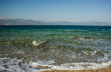 Aegean sea summer scenic landscape in Greece with waves near waterfront and mountain ridge background 