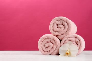 Obraz na płótnie Canvas Rolled soft towels with beautiful flower on table against color background. Space for text