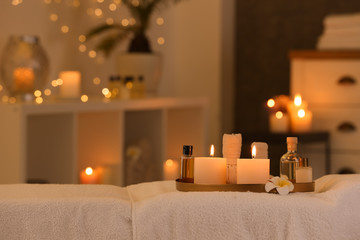 Cosmetics and burning candles on massage table in spa salon, space for text