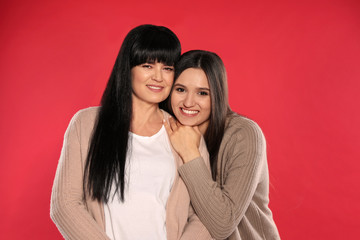 Portrait of young woman and her mature mother on color background
