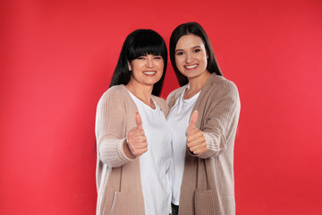 Young daughter and her mature mother showing thumbs up on color background