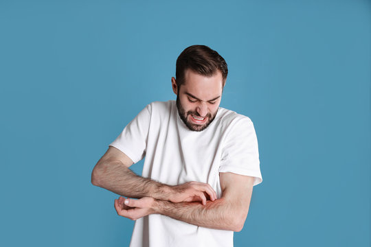 Young Man Scratching Hand On Color Background. Allergies Symptoms