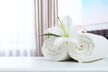 Fototapeta na wymiar Rolled towels and flower on table in bedroom. Space for text