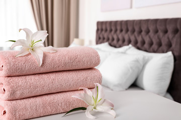 Stack of fresh towels with flowers on table in bedroom. Space for text