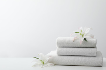 Obraz na płótnie Canvas Stack of fresh towels with flowers on table against white background. Space for text