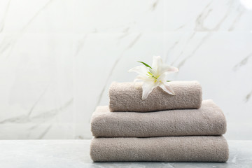 Stack of fresh towels with flower on grey table against light background. Space for text