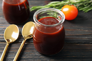Glass jar of barbecue sauce and spoons on wooden table