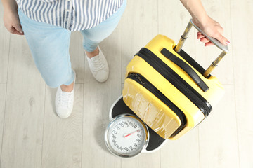 Woman weighing modern suitcase indoors, top view