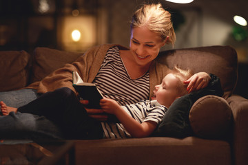 Family before going to bed mother reads to her child son book near a lamp in   evening.