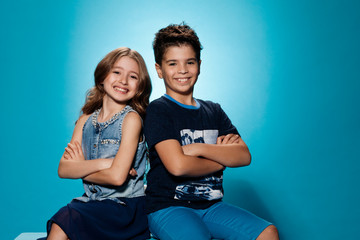 Children's fashion. Beautiful boy and girl in elegant clothes funny and posing together at studio over blue background. - Image