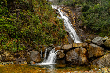 Beautiful landscape view of waterfall flowing around rocks with greens and stones.