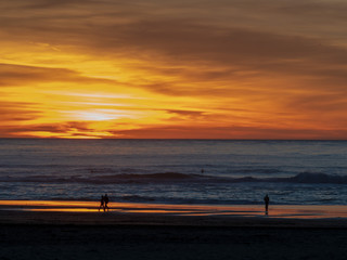 Sunset during dusk over Pacific Ocean with couples, surfers, and walkers
