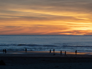 Fototapeta na wymiar Beach visitors walking along Pacific Ocean with sun setting during dusk 