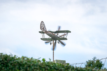 Weather vane in form of an old rusty biplane at a back angle, with propellers moving