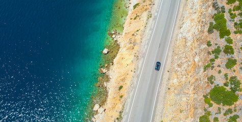 Fototapeta na wymiar TOP DOWN: Car cruises down the empty road leading along beautiful rocky beach.