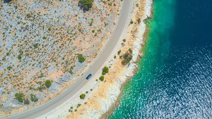 DRONE: Flying above tourist car driving along the beautiful glistening ocean.