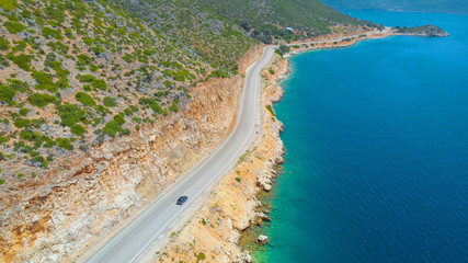 AERIAL: Flying over the emerald ocean as car cruises along the coastal road.