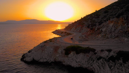 Fototapeta premium DRONE: Car drives down the asphalt road leading along the beautiful shoreline.