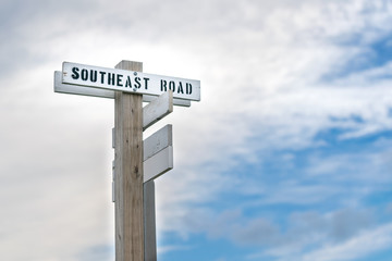Fototapeta premium Old wooden signpost with a simple black and white street sign, pointing the way to the Southeast Road, Block Island, RI