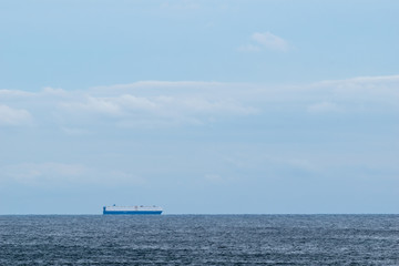Cargo ship on calm water, crossing the horizon on a beautiful sunny day