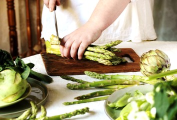 the woman's hands cut a bunch of asparagus. cooking in the kitchen at the table, on which lie...