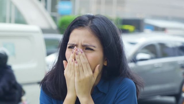 Air Pollution Concept. Woman coughing and closing her mouth while standing on the roadside in the city. Shot in 4k resolution